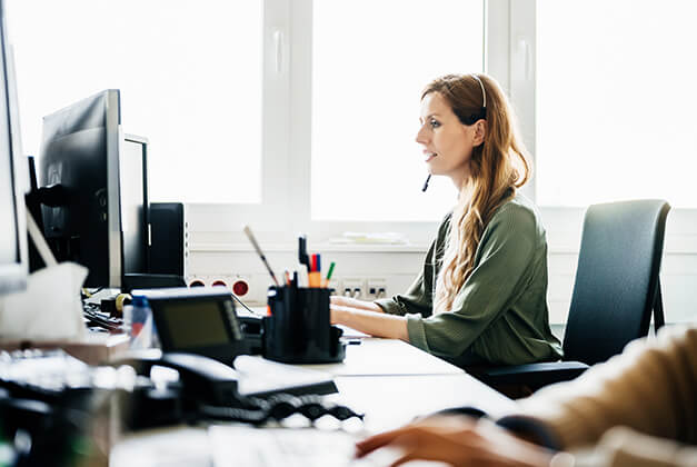 Frau mit aufgesetztem Headset vor einem Computer.