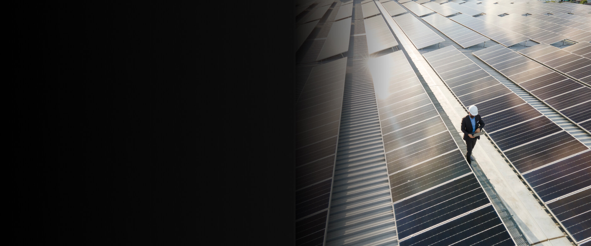 Business person with hard hat walking next to solar panels 