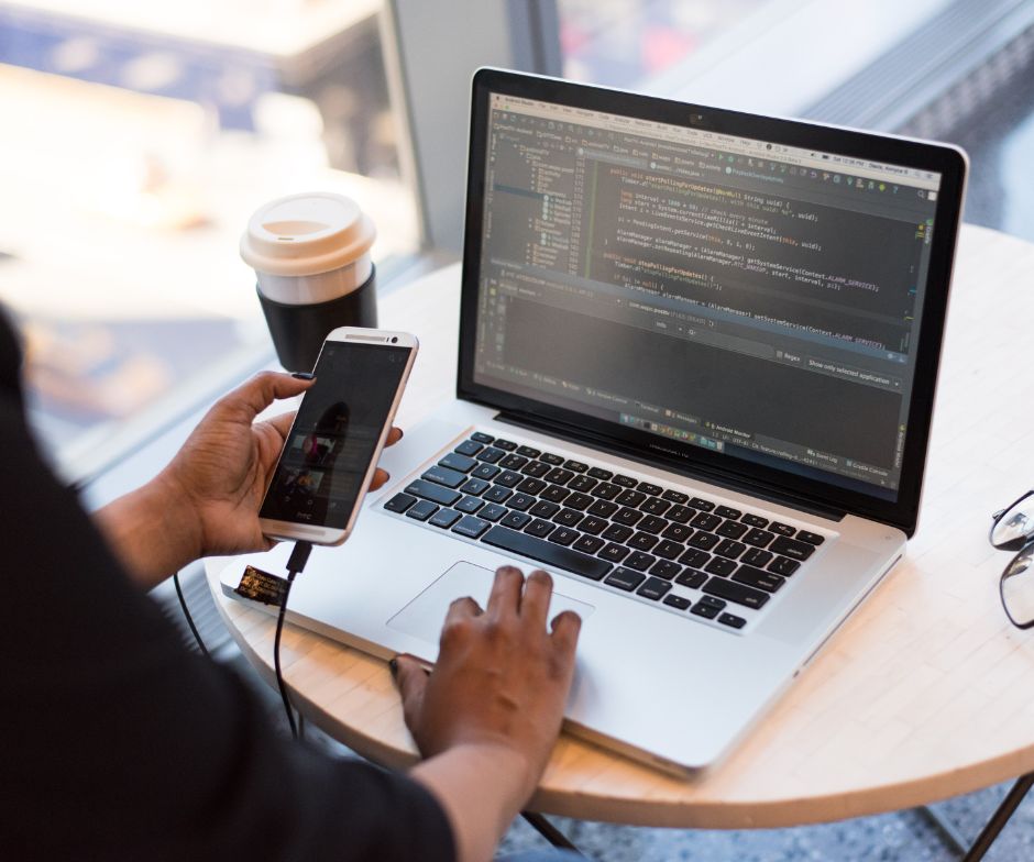 person working on his laptop while looking at the phone and coffee cup on the table