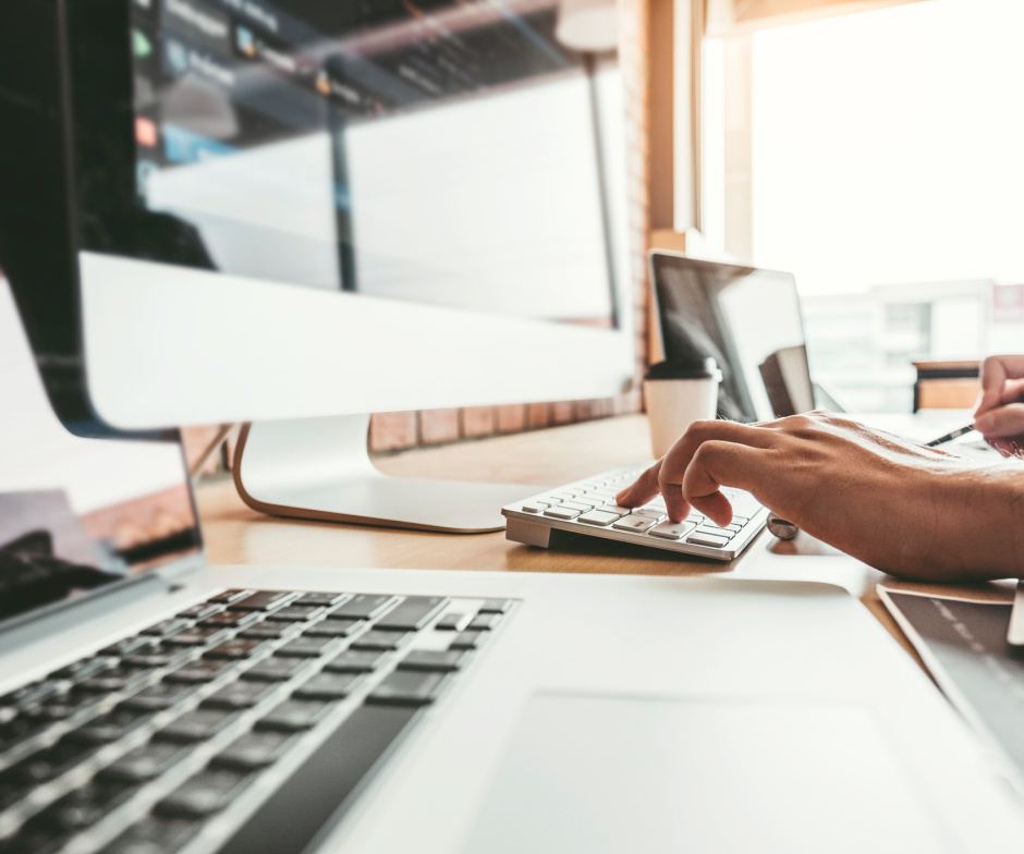 person typing on keyboard with in front of external monitor  and coffee cup on table